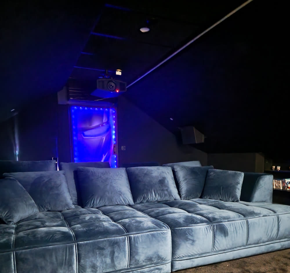 Ambiance de la salle de cinéma privée de Steven, éclairage tamisé bleu, grand canapé face à l'écran